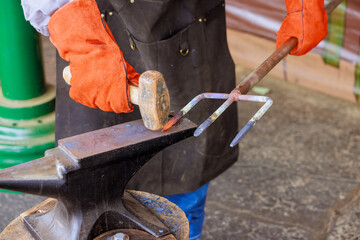 Blacksmith uses hammer to shape heated metal into garden fork while wearing protective gloves.