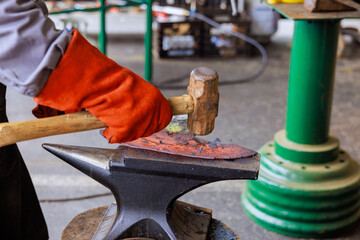 Craftsman shapes metal on an anvil using hammer in during axe making workshop setting.