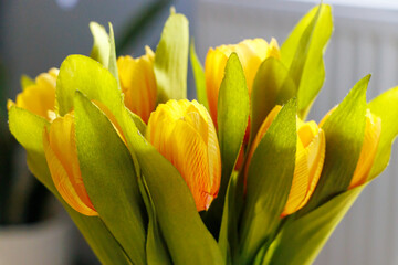 A vibrant bouquet of artificial yellow tulips with green leaves in a bright indoor setting, ideal for home decor and spring themes.