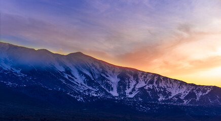 Obraz premium highland mountain landscape of beautiful sunset or sunrise behind nice mountain peaks and slopes in snow and majestic cloudy sky on background