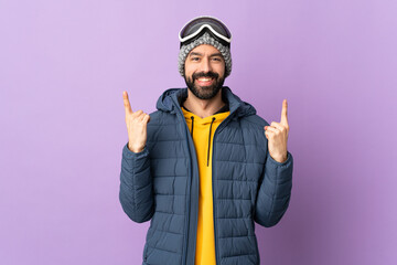 Skier man with snowboarding glasses over isolated purple background pointing up a great idea
