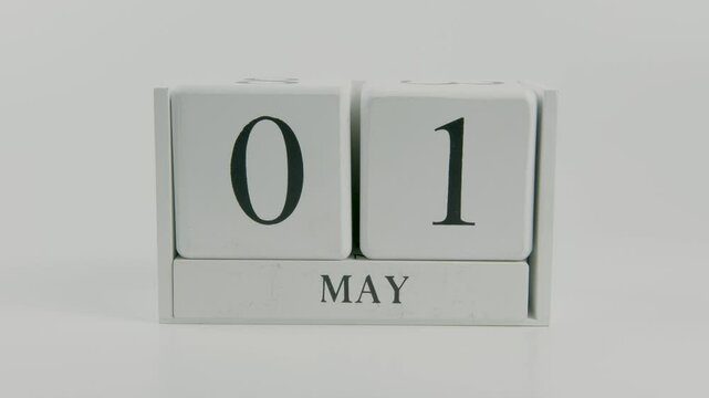 A hand flips a wooden calendar from 1st to 2nd June, symbolizing the passing of time and the change of the day, set against a white background