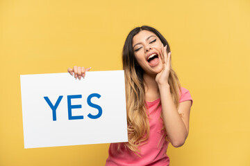 Young Russian girl isolated on yellow background holding a placard with text YES and shouting