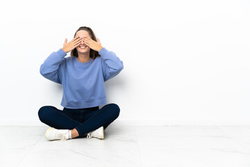 Young woman sitting on the floor covering eyes by hands and smiling