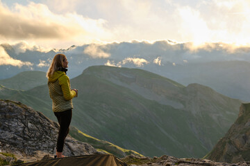 Woman with coffee mug admiring cloudy sunset and mountains