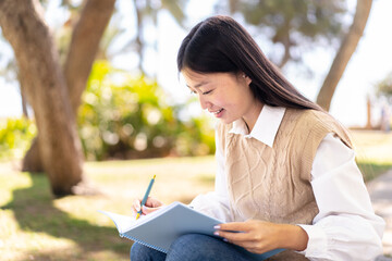 Fototapeta premium Pretty Chinese woman at outdoors holding a notebook