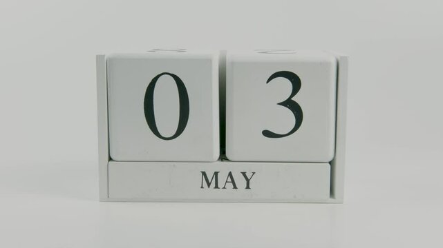 A hand flips a wooden calendar from 3rd to 4th June, symbolizing the passage of time on a white background