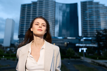 Confident businesswoman in urban setting, dressed in stylish attire exuding professionalism and poise, showcasing cityscape background during twilight, symbolizing ambition and success.