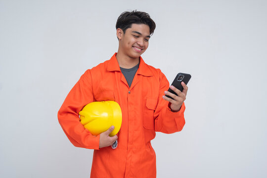 Young Southeast Asian male worker smiling while holding a phone, symbolizing sending remittance money to family through mobile banking. Isolated on a light background.