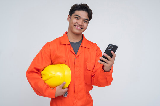 Happy Southeast Asian construction worker smiling while holding a phone and helmet, representing successful money transfer via remittance app.