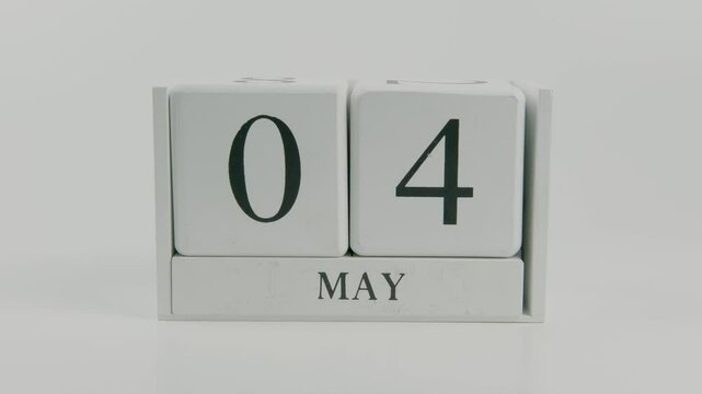 A hand flips a wooden calendar from May 4th to May 5th on a white background, symbolizing the smooth transition of time and a new day ahead