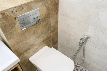 modern bathroom features a white toilet, a chrome flush plate, a bidet sprayer, and tiled walls in...
