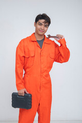 Young Southeast Asian male mechanic in orange coveralls holding a wrench and a tool case, ready for...