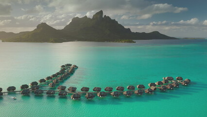 Stunning drone footage overwater bungalows lining a vibrant turquoise lagoon, mount Otemanu rising majestically in background, tropical paradise in Bora Bora. Travel exotic landscape vacation concept