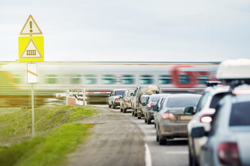 A queue of cars is waiting for a passenger train to travel at a railway crossing outside the city....