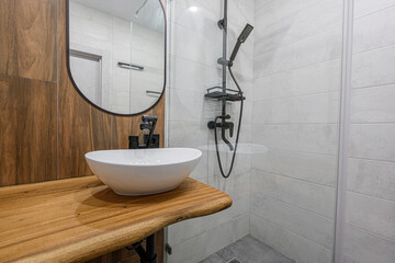 Modern bathroom featuring a white vessel sink on a wooden countertop, accented by a black faucet and mirror. Shower with white tile and black fixtures visible