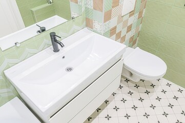 modern bathroom featuring a white sink with a dark faucet, a toilet, and patterned tiles. The walls are adorned with green and mosaic tiles, creating a fresh and stylish space.
