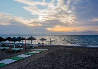 White soft sun loungers on the shore of a sandy sea beach. Tropical resort, morning sun, white clouds in the blue sky, view of the sea, mountains and the city in the background