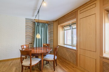 Warm dining area featuring a round wooden table with chairs, window with blinds, and paneled wooden...
