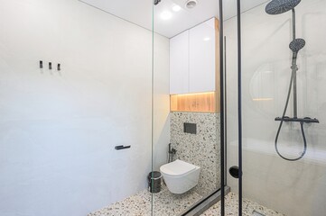 Modern bathroom with glass shower, wall-mounted toilet, and terrazzo flooring. Clean lines and minimalist design