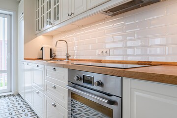 Bright kitchen with white cabinets, wood counters, stainless steel oven, and glossy white tile...