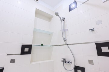 Modern bathroom shower area. White and black tiles, glass shelves, and a chrome shower fixture....