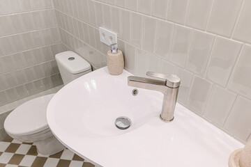 clean bathroom featuring a white sink with a modern faucet, a toilet, and light grey tiled walls. A...