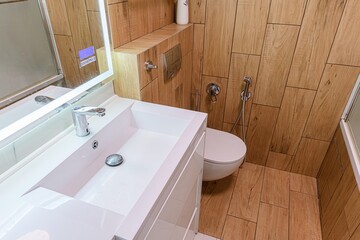 modern bathroom with wood-like tiled walls, a white sink, a lighted mirror, and a toilet.