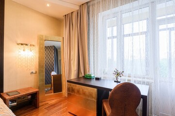 cozy room features a dark wood desk with gold accents, a full-length mirror, and a window with...