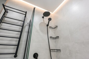 Modern bathroom corner featuring black fixtures: a showerhead, handheld shower, towel rack, and...
