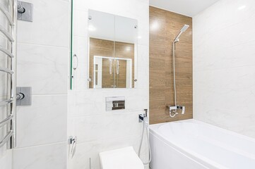 modern bathroom with white marble tiles, a wooden-look accent wall, bathtub, toilet, and mirrored cabinets