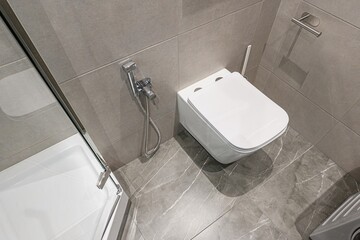 Modern bathroom featuring a white toilet, grey marble-like tiles, and a bidet shower, creating a...