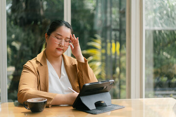 Asian Businesswoman A woman in a cozy cafe setting appears deep in thought while using a tablet,...