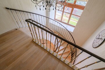 Elegant staircase with wooden steps, a dark handrail, and intricate metal railings. A chandelier...