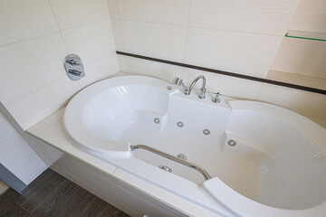 high-angle shot showcases a pristine white bathtub with silver fixtures, framed by light-colored, textured tiles