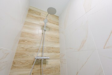 close-up of a shower with a chrome fixture. The walls are tiled, one side with a wood grain...