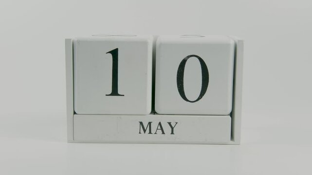 A hand flips a wooden calendar from May 10th to May 11th on a white background, symbolizing the passing of time and the arrival of a new day