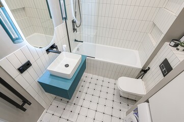 modern bathroom featuring white tiles, a turquoise vanity, a white sink, toilet, and patterned floor. Black fixtures accent the bright space