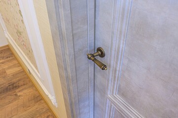 close-up of a light gray paneled door with a bronze handle, hallway interior, and floral wallpaper...