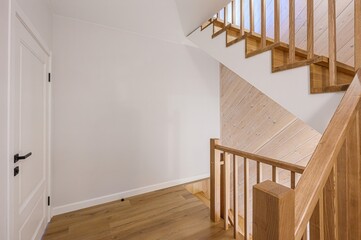 bright, modern interior featuring a staircase with wooden steps and railings. A white door with...