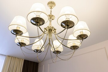ceiling shot shows a chandelier with eight lamps, each with a white shade. It hangs against a white...