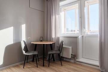 Cozy dining area with a round table, two gray chairs, and natural light streaming through a window with light curtains