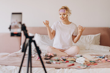 Smiling blonde young teenager applying skin care patches, recording video for vlog in bedroom