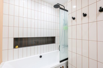 Modern bathroom with white tiles, black fixtures, and a built-in niche featuring a rubber duck....
