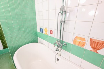 bright bathroom with mint green and white tiles. Features a pink ceiling and a chrome shower fixture. Child-like drawings decorate the tiles.