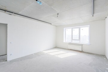 empty, unfinished room with white walls and a concrete floor. Pipes run along a concrete ceiling