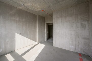 Bare, light-filled room in renovation with exposed concrete ceiling, plastered walls, and smooth...