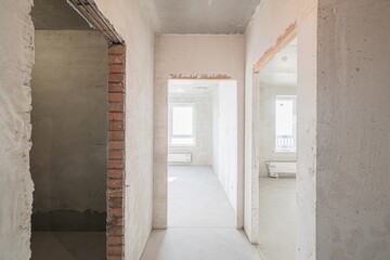 Bare, light-filled room in renovation with exposed concrete ceiling, plastered walls, and smooth...