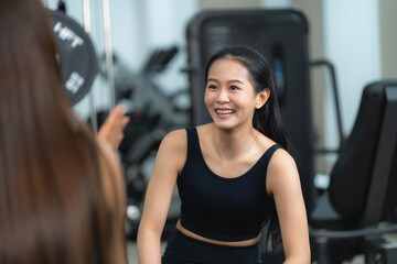 Fototapeta premium Two Asian women talking and relaxing after a workout session at the gym. Concept of healthy lifestyle, fitness friendship, and post-exercise recovery.