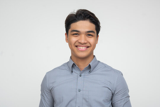Confident young Southeast Asian man smiling directly at camera, expressing positivity and friendliness. Isolated on a light background.